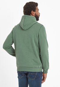 Green hooded sweatshirt with a smooth texture, ribbed cuffs and hem, and a relaxed fit, paired with blue jeans.