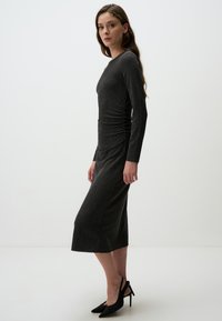 Abito grigio attillato a maniche lunghe con texture a costine e dettaglio arricciato in vita. Indossato con décolleté slingback nere a punta.