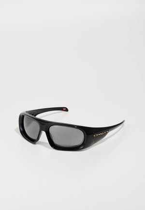 Černé oblé sluneční brýle Oakley s obdélníkovými šedými skly a zlatým logem na spánku, na bílém pozadí.