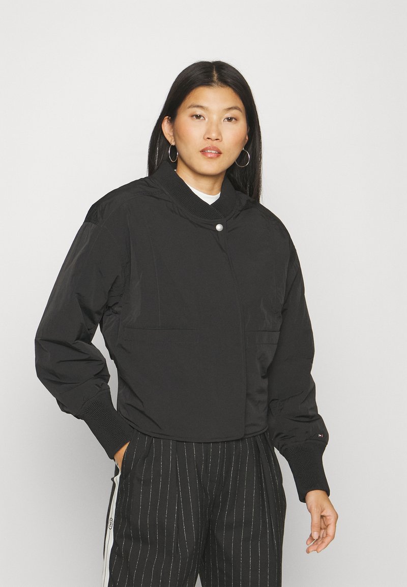 Black bomber jacket with a high neckline, front snap closure, and side pockets. Features ribbed cuffs and a smooth, matte finish.