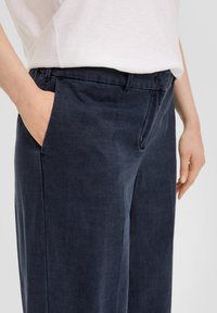 Marineblauwe broek met een ontspannen pasvorm, voorzien van zijzakken en een soepele, textuur vol stof. De tailleband is op maat gemaakt met riemlussen.