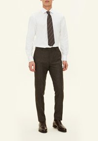 Camicia bianca a maniche lunghe, pantaloni grigi scuri con una finitura testurizzata e una cravatta marrone a righe. Scarpe da uomo in pelle marrone completano il completo.
