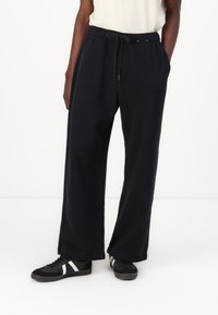 Črne trenirka made iz mehkega blaga, z elastičnim pasom in vrvico, ter stranskimi žepi, zasnovane v ohlapnem kroju.