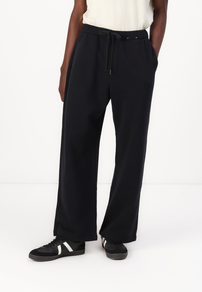 Črne trenirka made iz mehkega blaga, z elastičnim pasom in vrvico, ter stranskimi žepi, zasnovane v ohlapnem kroju.