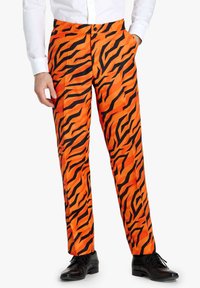 Pantaloni arancioni con un motivo a strisce nere a tigre, con design a vita piatta, tasche laterali e vestibilità sartoriale, abbinati a scarpe nere.