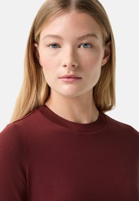 Burgundy long-sleeve shirt with a crew neckline, smooth texture, and fitted design, highlighting clean lines and a minimalist look.