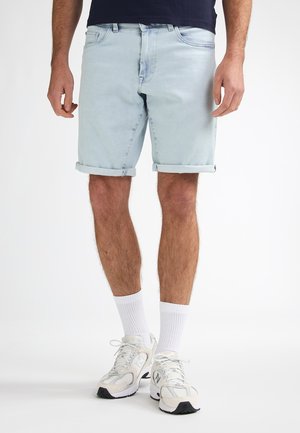 Lichtblauwe denimshorts met opgerolde pijpen, voorzien van een klassiek ontwerp met vijf zakken en een taillehoogte halverwege, gecombineerd met witte sportschoenen.