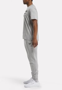 Grijze t-shirt met korte mouwen en zwart logo, gecombineerd met grijze sweatpants. Witte sneakers met subtiele details. Eenvoudig, atletisch ontwerp.