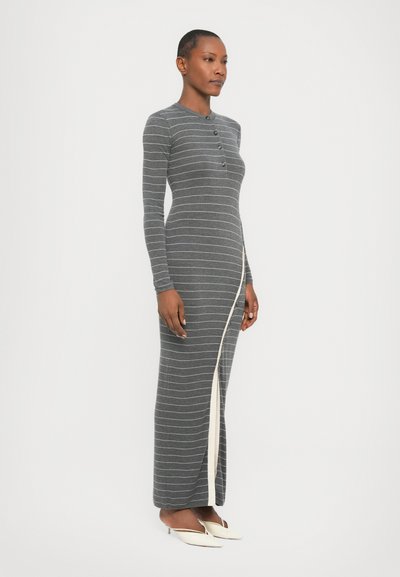 Dark gray long-sleeve dress with white horizontal stripes, featuring a buttoned neck and a side slit with contrasting trim. Worn with white heels.