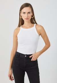Top de tirantes blanco acanalado con un escote alto y tirantes finos, combinado con jeans negros de cintura alta. Diseño sencillo, textura suave.
