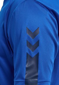 Blå idrottströja med strukturerad tyg, korta ärmar och ett glansigt mörkblått triangulärt mönster på överarmen.