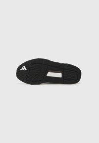 Semelle de chaussure de sport noire avec grip en caoutchouc texturé, ornée d'un accent argenté et de la marque "TRAXION". Motif de traction distinct pour la stabilité.