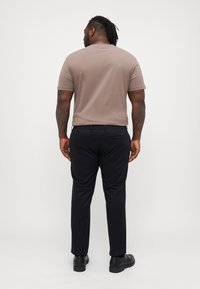 Tricou scurt maro, cu mânecă scurtă și guler rotund, asortat cu pantaloni negri drepti și pantofi negri, văzut din spate.