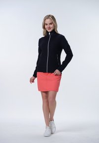 Mörkblå zip-up jacka med hög krage, tillsammans med en korallfärgad kjol. Outfiten kompletteras av vita sneakers. Enkel och modern design.