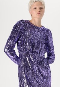 Vestido roxo de lantejoulas com mangas longas, franzido à cintura. Apresenta uma textura suave, brilhantes embellishments e um decote redondo.