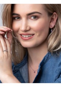 Zilveren oorbellen met paarse edelstenen, een bijpassende ketting en een zilveren ring. Het model draagt een spijkerjack, met lichtbruin haar en natuurlijk make-up.