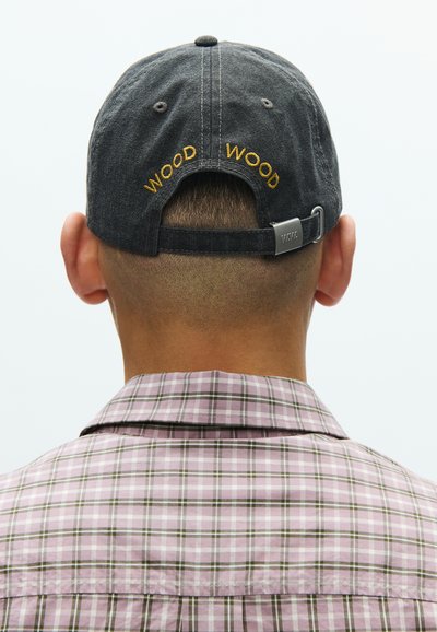 Ρυθμιζόμενο μαύρο καπέλο από ύφασμα με κεντημένο κίτρινο "WOOD" στο πίσω μέρος. Παρουσιάζεται ένα πουκάμισο καρό σε απαλούς ροζ, πράσινους και λευκούς τόνους.
