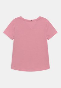 Kort lyserød T-shirt lavet af blød bomuld med korte ærmer, rund hals og buet kant. Har en diskret V-hals detalje.
