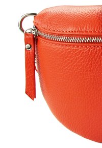 Ronde oranje leren tas met een zilveren rits, een gestructureerd oppervlak en een bevestigde leren trekhaak voor gemakkelijke opening.