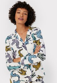 Vit pyjamasfynd med färgglada krokodilillustrationer i blått, gult och lila. Knappar ned design med bröstficka.