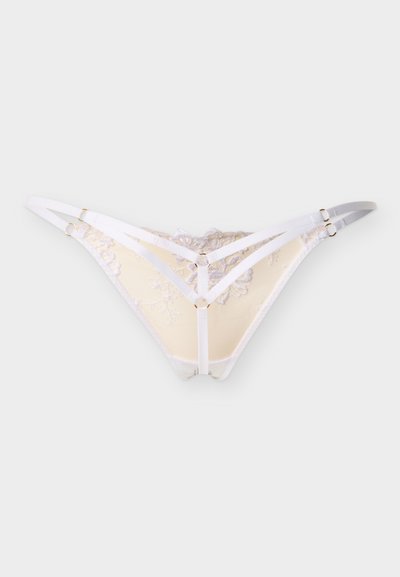 Λευκό σλιπ από δαντέλα με λουλουδάτη κεντητική, διπλές πλαϊνές λωρίδες και μεταλλικούς κρίκους σε χρυσό τόνο σε φωτεινό φόντο.