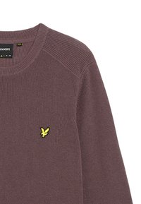 Bruine geribbelde trui met ronde hals en gele geborduurde logo op de borst. Heeft een textuurstof en raglanmouwen voor comfort.
