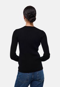 Pull noir côtelé à manches longues avec col rond, design fitted et tissu texturé, associé à un jean en denim bleu.