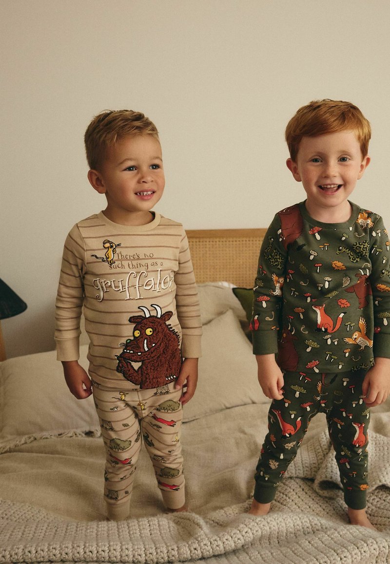 Deux enfants portent des pyjamas ludiques. L'un a des rayures beiges avec un graphique du "Gruffalo" ; l'autre est en tissu vert avec des motifs d'animaux colorés.