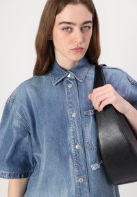 Ανοιχτό μπλε τζιν πουκάμισο με κοντά μανίκια, κούμπωμα με κουμπιά και τσέπη. Μαύρη δερμάτινη τσάντα με κυρτή θηλιά. Απαλή υφή, χωρίς ορατά μοτίβα.