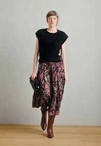 Czarna krótka sweterkowa bluzka z krótkim rękawem zestawiona z długą spódnicą w kwiatowy wzór. Dopełnieniem stroju są brązowe kowbojki do kolan i czarna kopertówka.