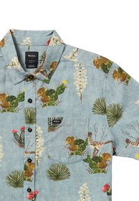 Mønstret t-shirt med korte ærmer i lyseblåt stof, med blomster- og ørkenplante-motiver, med en brystlomme og sort knaplukning.