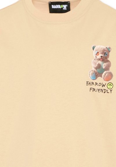 Chemise beige avec petit motif d'ours en peluche coloré et texte "BARROW FRIENDLY" sur le haut gauche de la poitrine, sous l'encolure.
