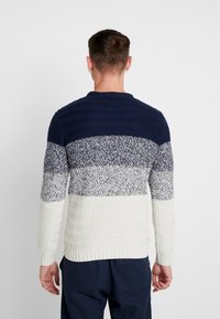 Marineblauwe, crème en grijze gebreide trui met een gestructureerd zigzagpatroon. Voorzien van geribbelde boorden en zoom, en een ronde hals.
