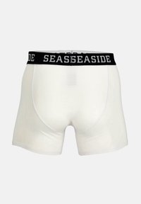 Boxers blancs avec une ceinture élastique noire sur laquelle est imprimé "SEASIDE" en blanc. Le design est lisse et ajusté.
