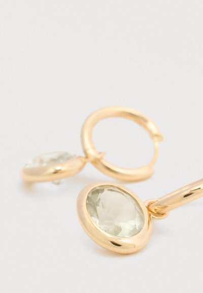 Cercei de tip cerc, placati cu nuanță aurie, cu pietre prețioase mari, clare și fatetate, însetate într-o montură netedă. Designul include o formă simplă și elegantă.