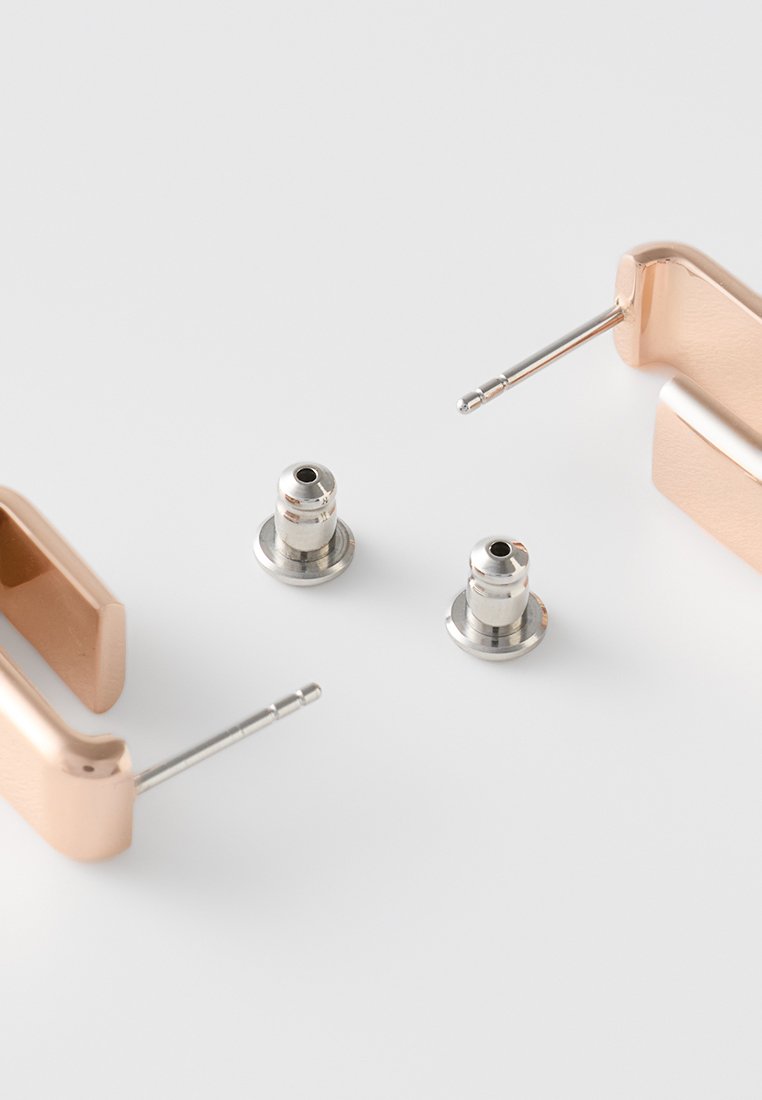 Roségoldene Metall-Ohrmuscheln mit silbernen Anschlüssen und Spitzen, ausgestattet mit einer glatten Oberfläche und einem eleganten Design, vor einem weißen Hintergrund.
