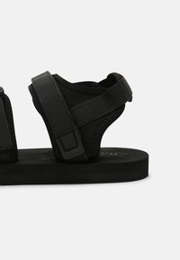 Sandales noires avec des sangles ajustables en tissu texturé, un semelle intérieure profilée et une semelle en caoutchouc plate, conçues pour le confort et le soutien.