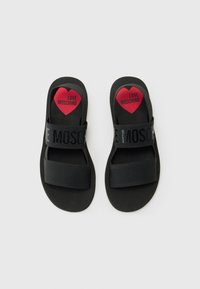 Mustat liukusandaalit, joissa on kaksi leveää remmiä. Toisessa remmissä lukee "LOVE MOSCHINO" mustilla kirjaimilla. Punainen sydänlogo sisäpohjassa. Sileä pinta.