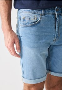 Light blue denim shorts with a rolled hem, front pockets, and visible stitching details. Fabric appears soft and slightly worn.