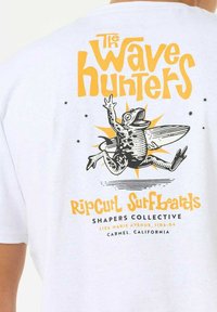 Hvid bomulds t-shirt med et sort-gult grafisk motiv af en frø med en surfbræt, tekst "The Wave Hunters" og brandingdetaljer.