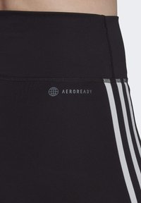 Czarne legginsy sportowe o gładkiej fakturze, z wysokim stanem i białymi paskami po bokach, z logo "AEROREADY" w kolorze szarym.