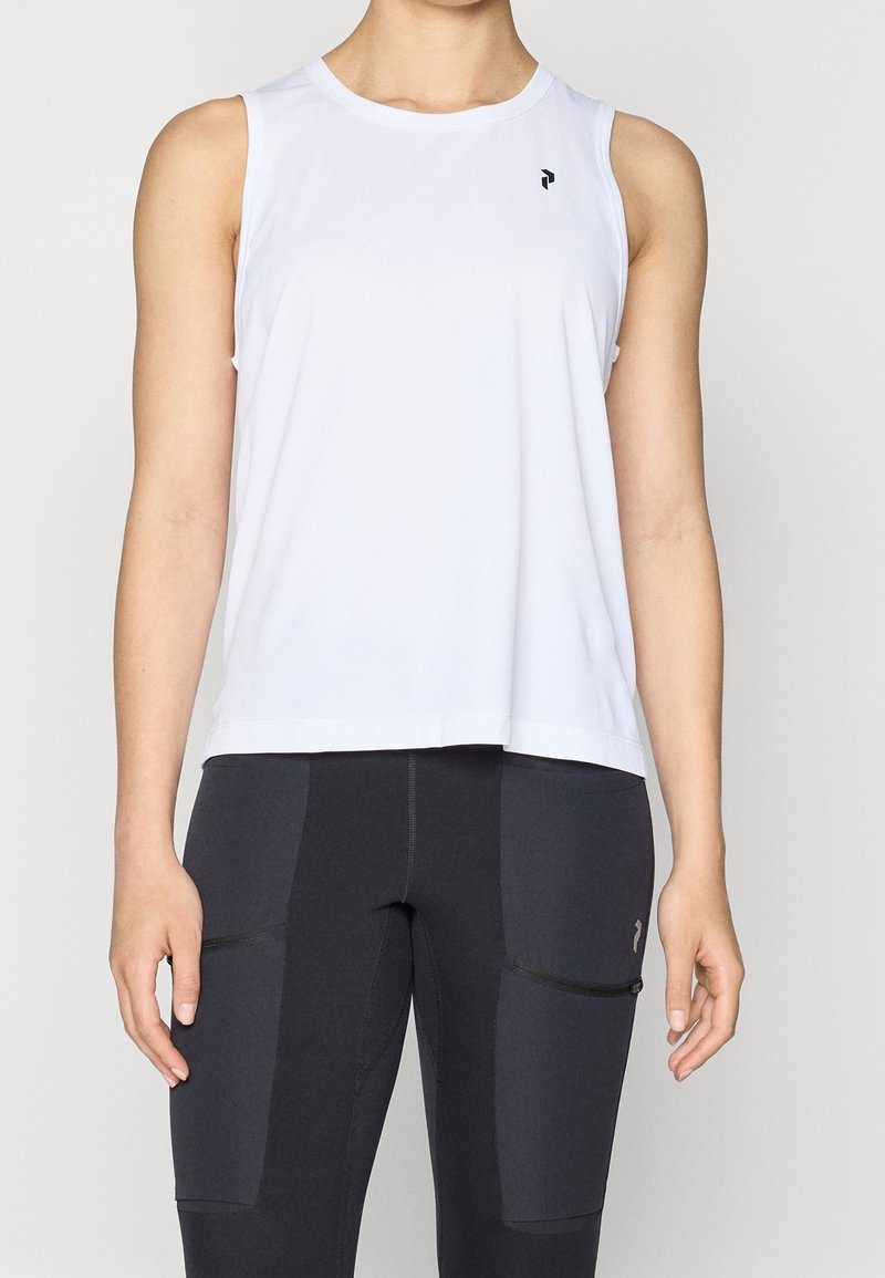 Femme portant un haut de sport blanc sans manches et un legging de sport noir avec des poches avant, vue du cou jusqu’aux hanches.