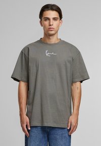 T-shirt en coton gris avec une coupe décontractée et des manches courtes. Présente un logo signature blanc sur la poitrine et un col rond.