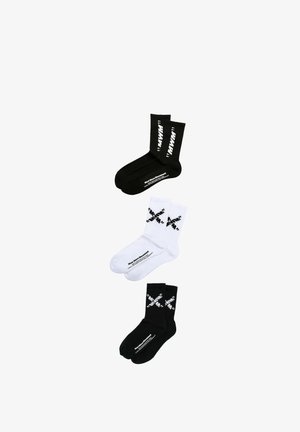 Tres pares de calcetines deportivos: uno negro con texto blanco, uno blanco con detalles gráficos negros y otro negro con elementos de diseño blancos.