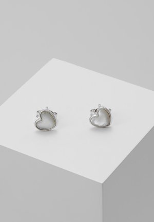 Boucles d'oreilles clous en forme de cœur en argent avec une incrustation lisse et brillante en nacre, présentées sur un socle blanc sur fond gris.