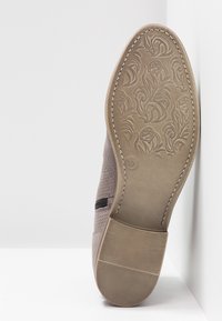 Gray shoe sole with textured floral pattern, reinforced heel, and flexible design. Features a side elastic panel for easier wear.