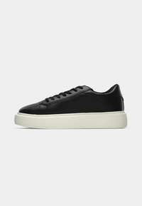 Black leather sneaker with a rounded toe, flat laces, and a white rubber sole featuring textured details. Smooth surface with minimal design.