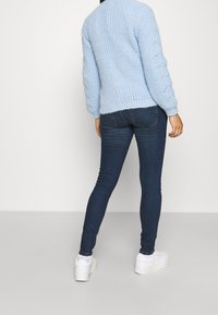 Svetle modrý pletený svetr s texturovaným vzorem a spadenými rameny, kombinovaný s tmavě modrými skinny džíny a bílými platformovými teniskami.