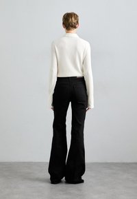 White, ribbed long-sleeve top paired with black, flared jeans. The outfit features a fitted silhouette and slightly oversized sleeves.