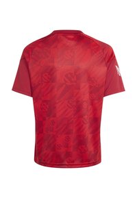 Κόκκινο αθλητικό κοντομάνικο jersey με διακριτικό γεωμετρικό σχέδιο και αχνά κυκλικά λογότυπα στην πλάτη, με στρογγυλή λαιμόκοψη και λευκό γραφικό στο δεξί μανίκι.